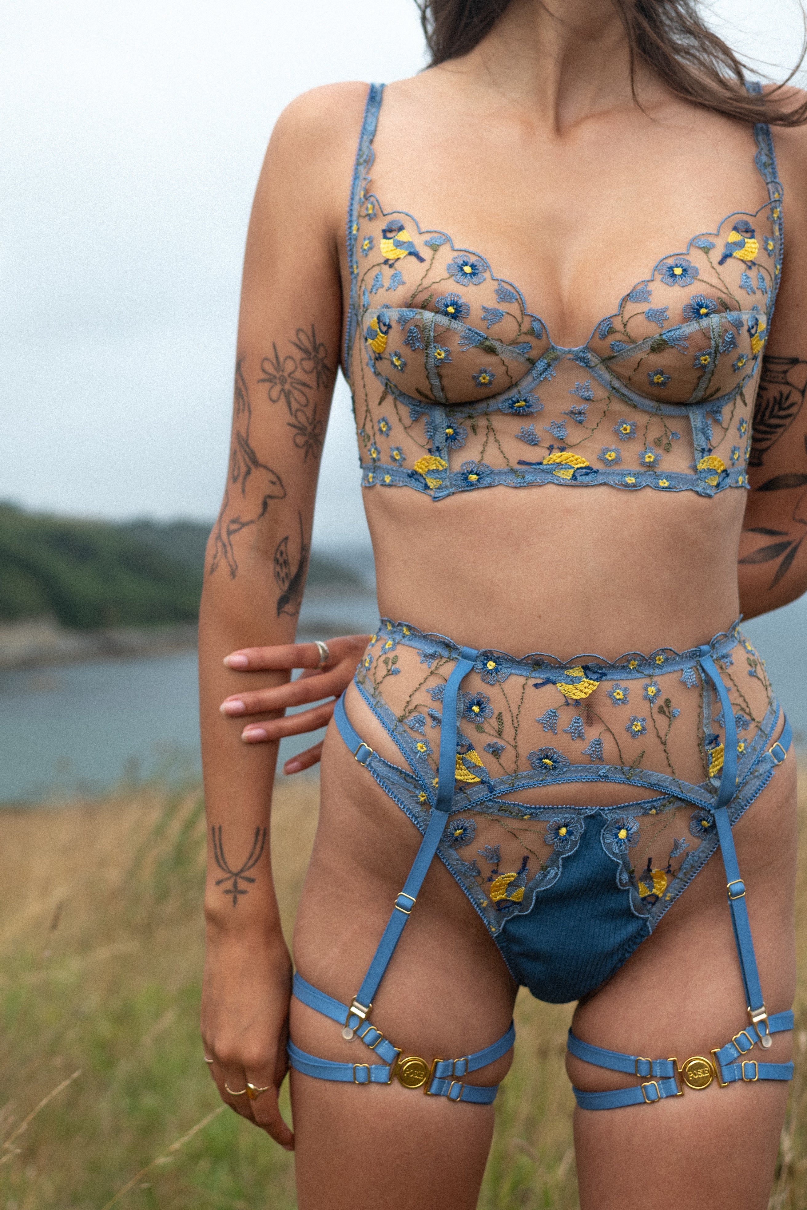 Model wearing a blue floral lingerie set with suspender belt outdoors.